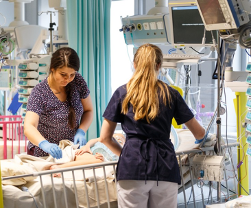 Dwie pielęgniarki wykonujące czynności pielęgnacyjne przy pacjencie na sali chorych