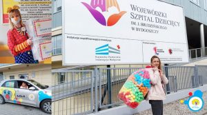 Pani klaun z darami dla dzieci przed Wojewódzkim Szpitalem Dziecięcym w Bydgoszczy, promująca radość i wsparcie.