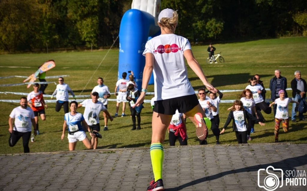 Biegacze na imprezie sportowej, kobieta w białej koszulce i zielonych skarpetkach przoduje w wyścigu.