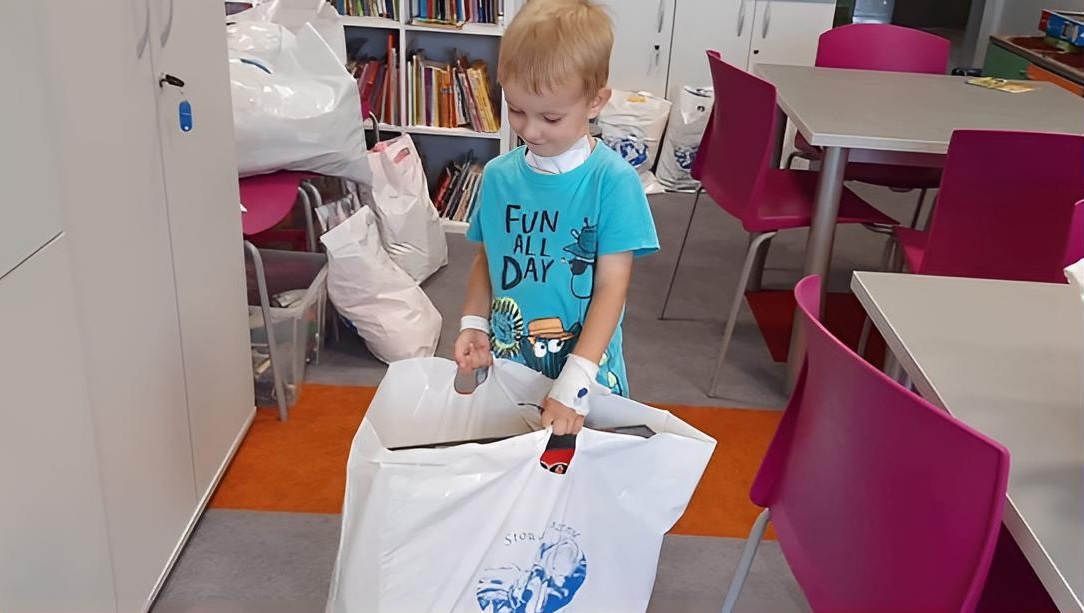 Chłopiec w szpitalnej sali szkolnej zagląda do torby z upominkami od Stowarzyszenia Łatwo Pomagać