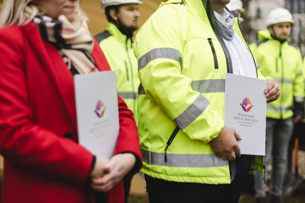Pracownicy w kamizelkach odblaskowych trzymają dokumenty związane z budową nowego szpitala dziecięcego w Białymstoku.
