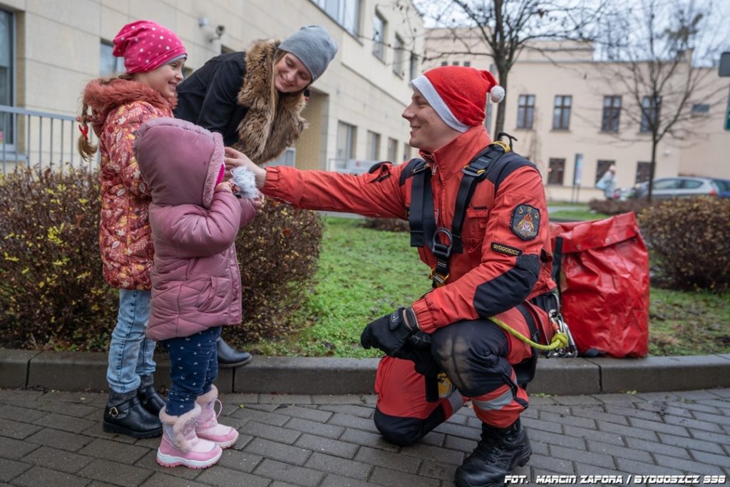 Ratownik w czerwonym stroju rozmawia z dwiema dziewczynkami podczas charytatywnego wydarzenia w Bydgoszczy.