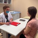 Lekarka w maseczce rozmawia z pacjentką w przyjaznej atmosferze podczas wizyty w gabinecie.