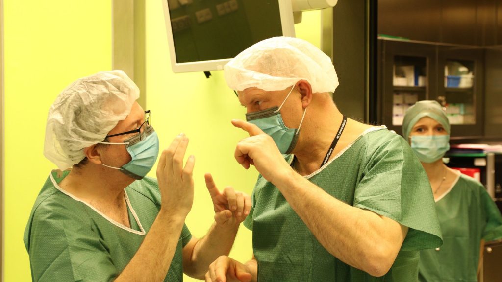 Lekarze w szpitalnej sali rozmawiają, przygotowując się do zabiegu chirurgicznego w zielonych fartuchach.