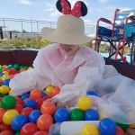 Dziecko w słomkowym kapeluszu z uszami Myszki Mickey bawi się kolorowymi kulkami w basenie.