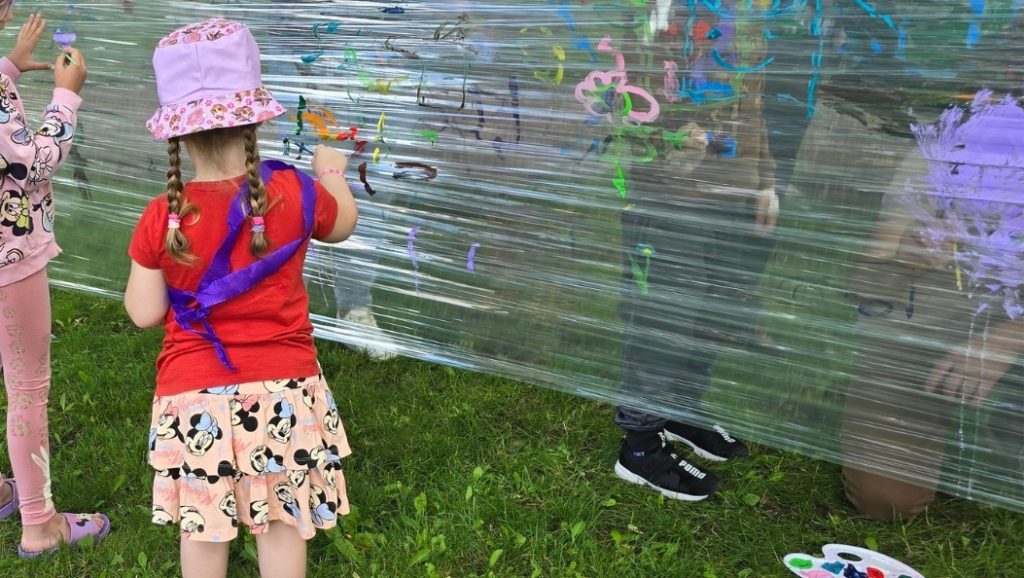 Dzieci podczas zajęć plastycznych w parku przyszpitalnym – kolorowe malunki farbami na folii stretch 
