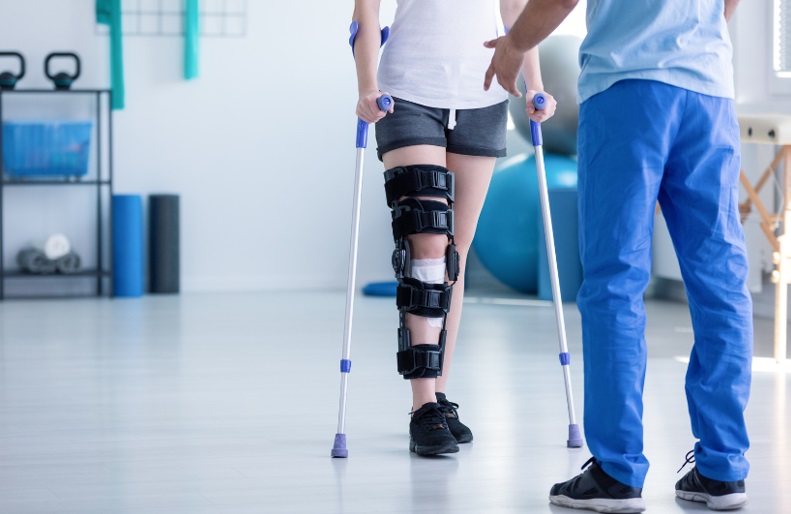 Rehabilitacja osoby z kontuzją kolana, korzystającej z kulek i ortozy w nowoczesnym centrum fizjoterapii.