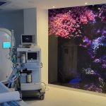 Nowoczesne wnętrze pracowni tomografii komputerowej z kolorowym muralem podwodnym i sprzętem medycznym.